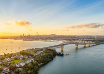 A panoramic image from above of Auckland, with the Sky Tower and CBD visible across Waitemata Harbor and the Auckland Harbour Bridge.