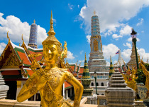 Wide angled view of Buddha sculpture Kinora or Kinnaree ( mythological creature, half bird, half man ) at Wat Phra Kaeo and Grand Palace in Bangkok, Thailand. Many details of Grand Palace in the background, also visible are beautiful cloudscape with blue 